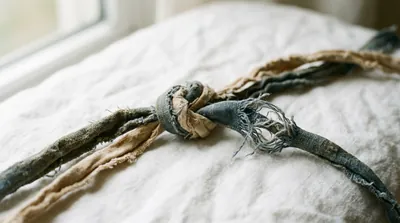 Two worn cords intertwined on white linen, one beginning to come loose, in soft natural light